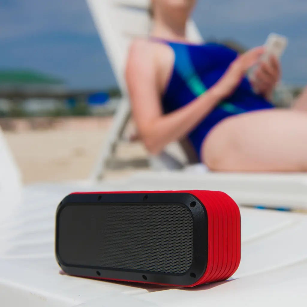A portable Bluetooth speaker on a lounger beside a sunbather