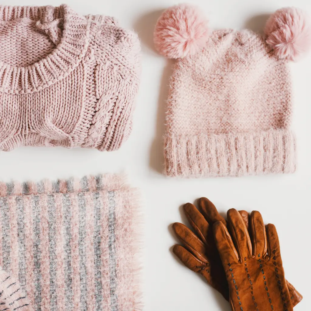 A knit sweater, pom-pom hat, scarf and leather gloves laid flat