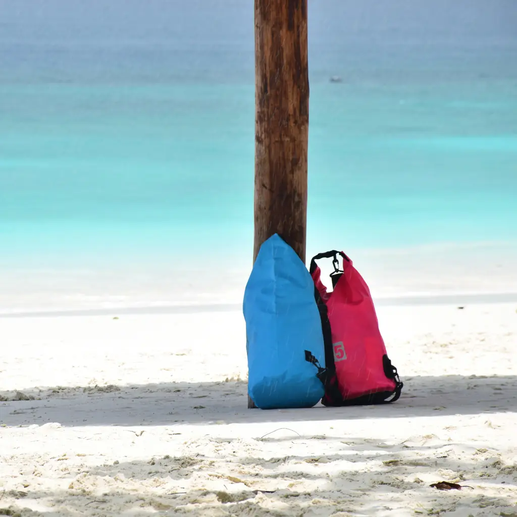 Two waterproof dry bags propped against a post on a white sand beach