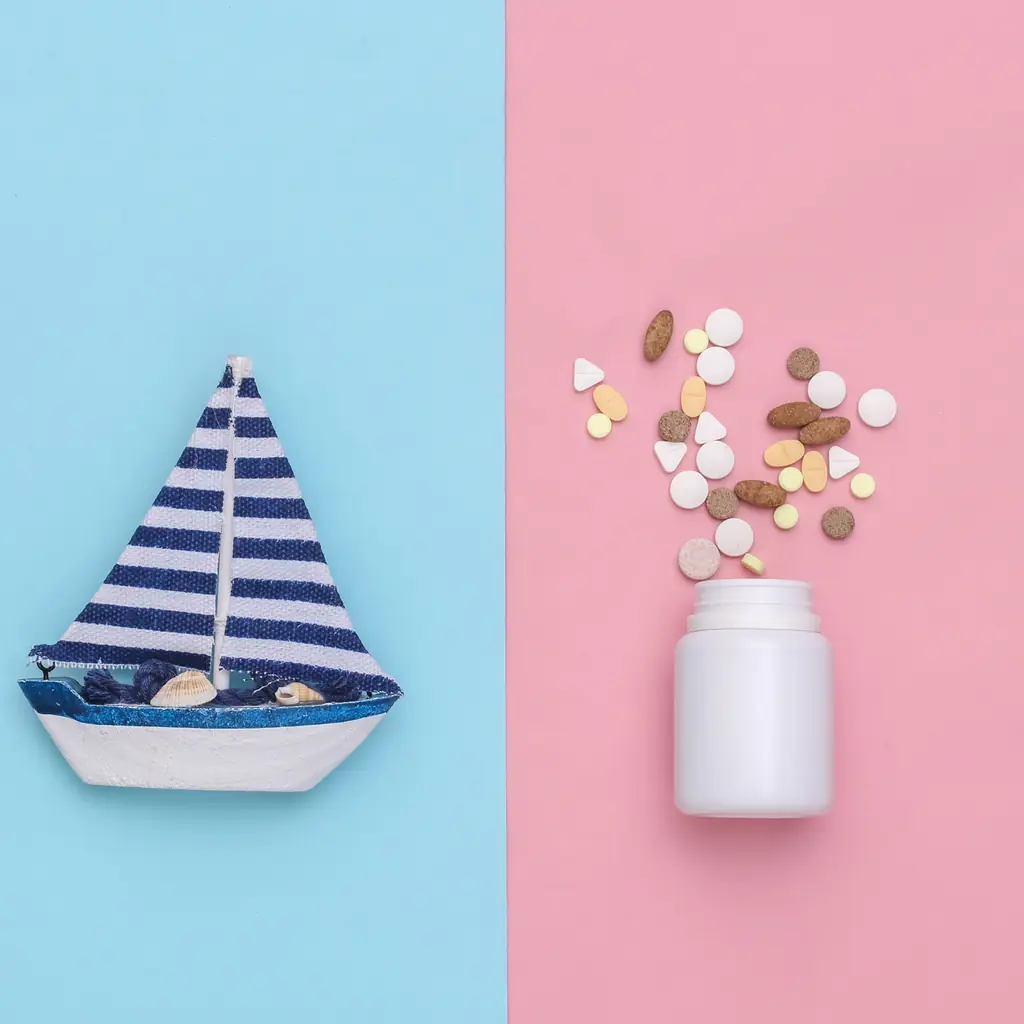 Seasickness tablets spilling from a bottle beside a toy sailboat