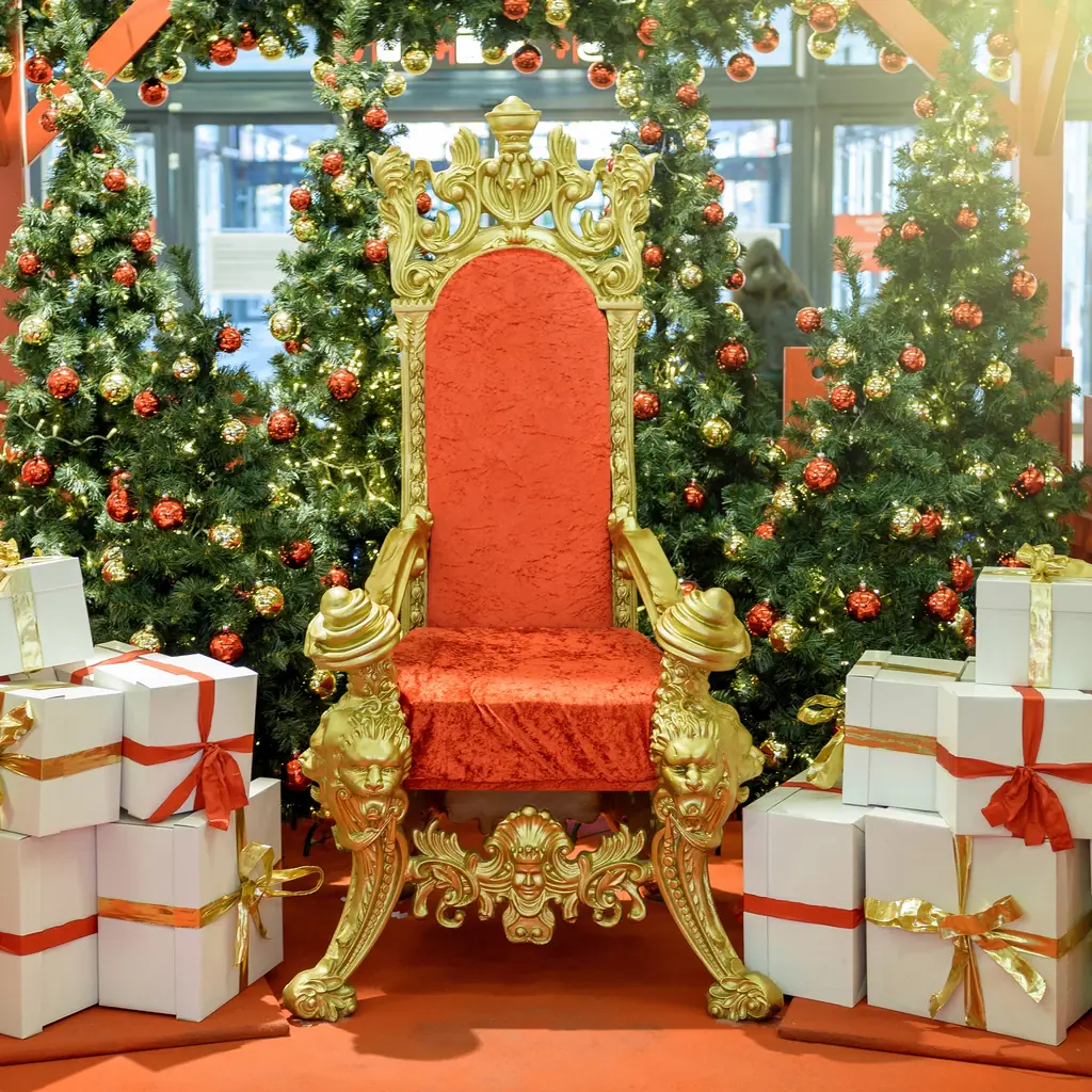 An empty Santa's throne surrounded by Christmas trees and wrapped gifts