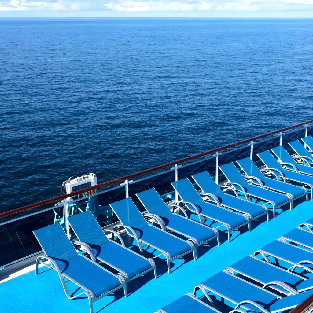 A cruise ship pool deck on a sea day with open ocean beyond the railings