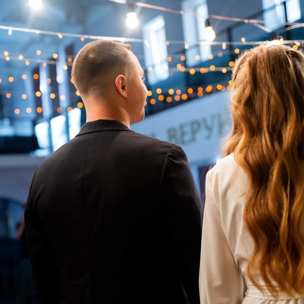 A dressed-up couple seen from behind under strings of party lights