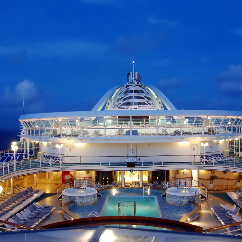 Cruise ship pool deck lit at night with empty loungers