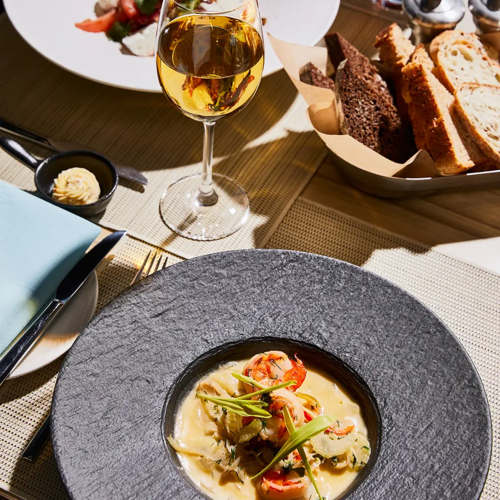 A starter of shrimp soup with bread and a glass of white wine on a set table