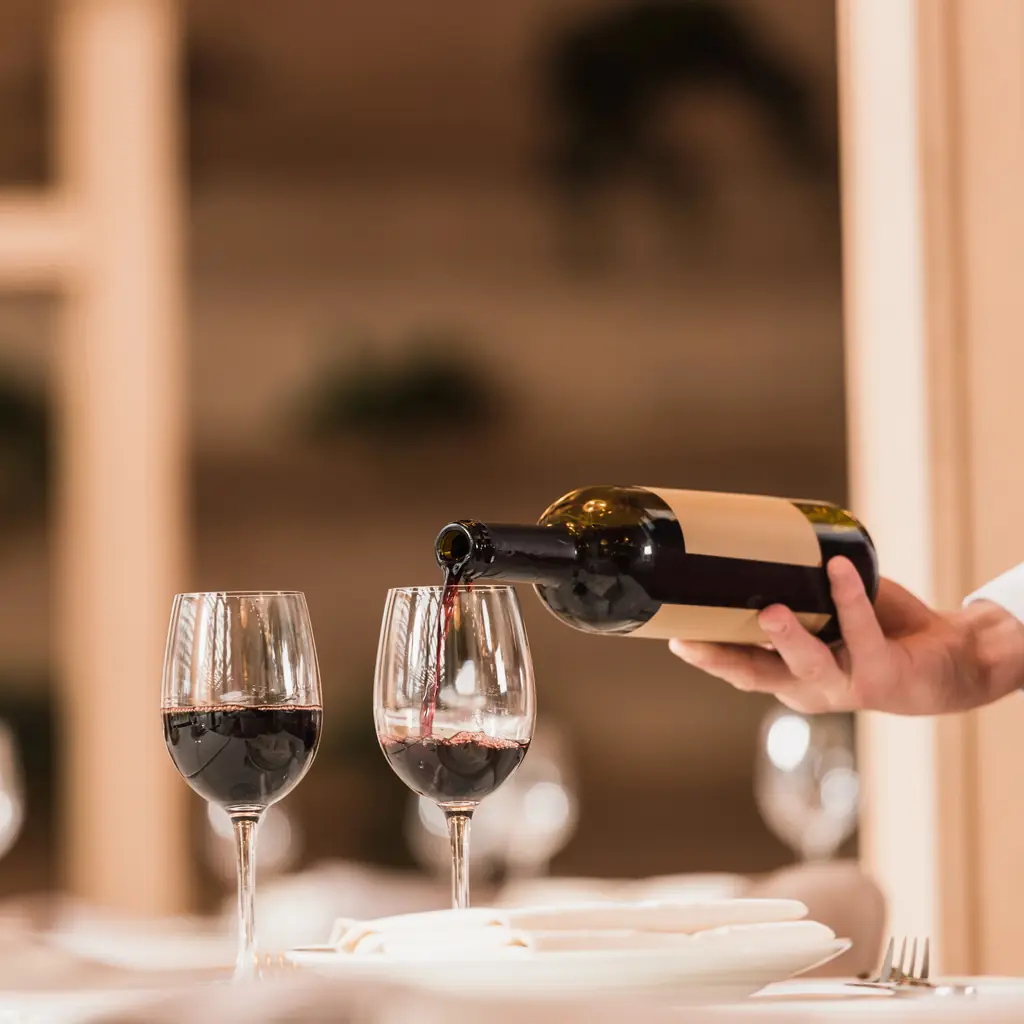 A waiter pouring red wine into glasses at a dinner table