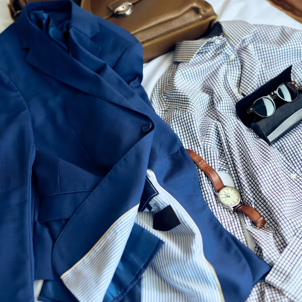A navy blazer, pressed shirt and watch laid out on a bed for the evening