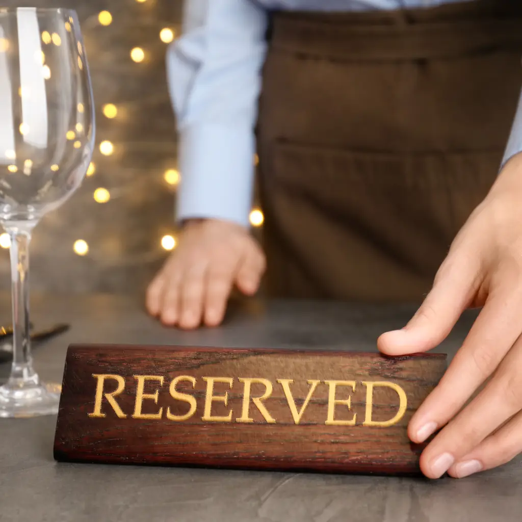 A waiter placing a reserved sign on a set dinner table