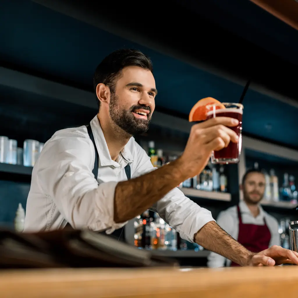 A bartender serving a cocktail across the counter of a cruise ship bar