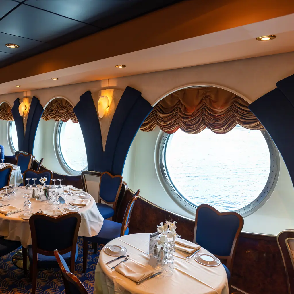 A table for two with wine set beside a window in a cruise ship specialty restaurant