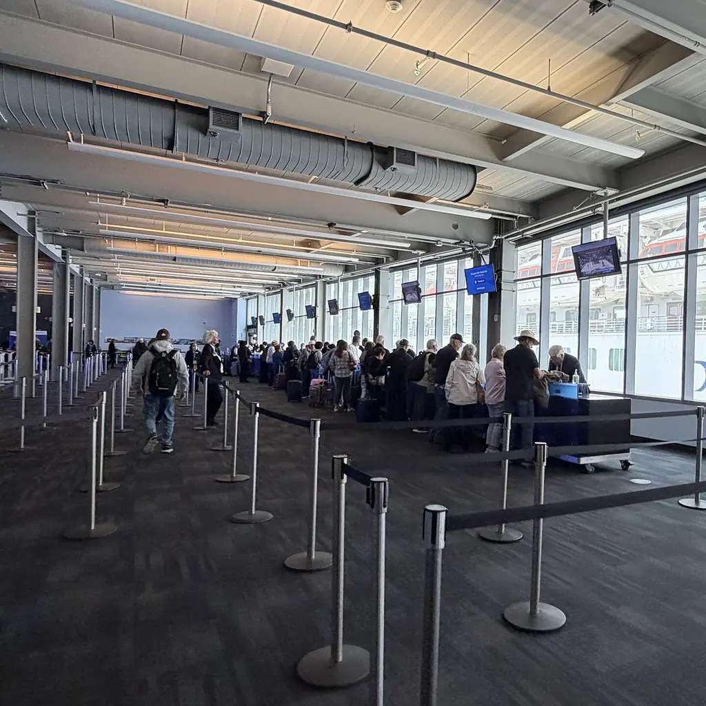 Passengers lining up in roped queue lanes inside a cruise terminal