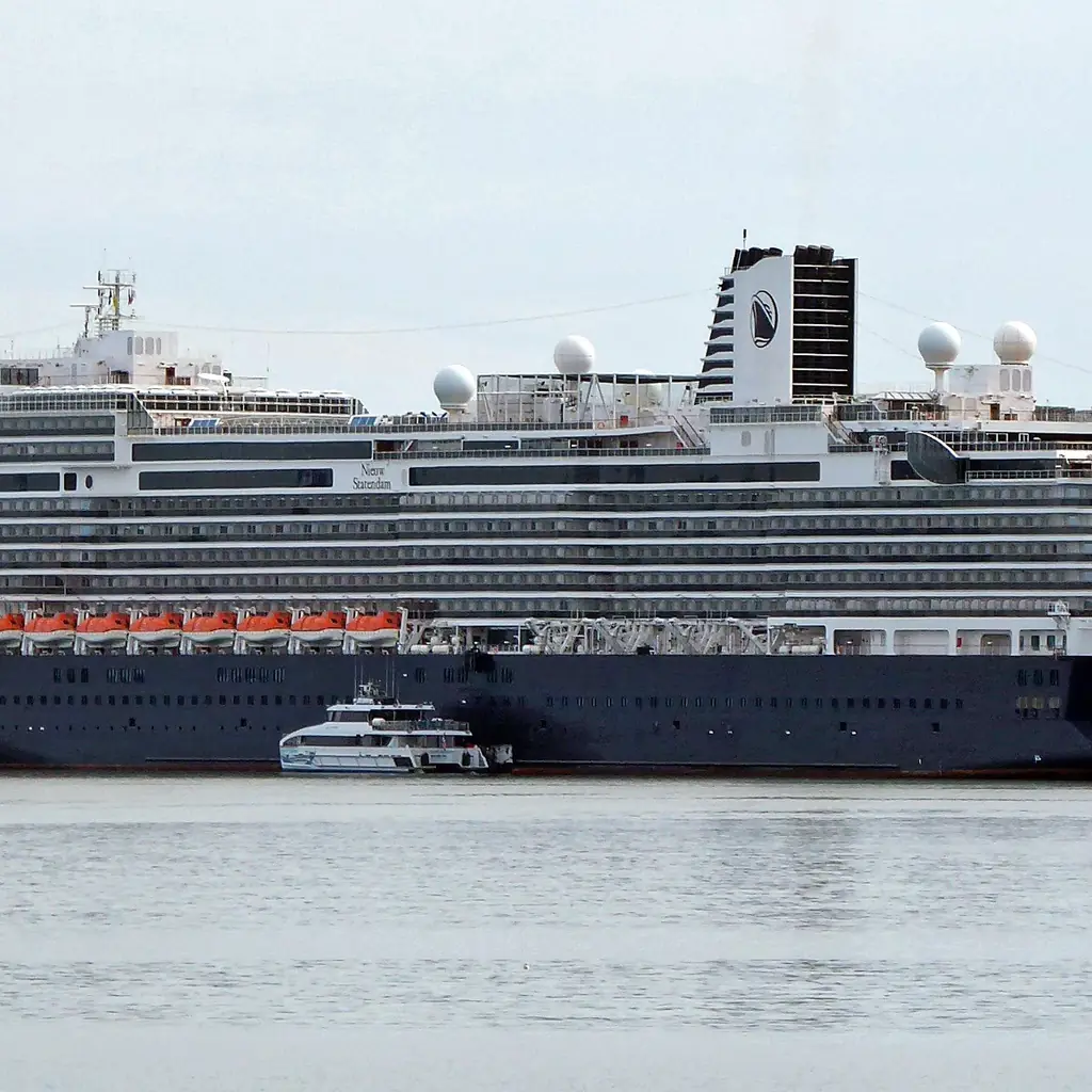 A Holland America Line ship with a dark blue hull docked at a cruise port