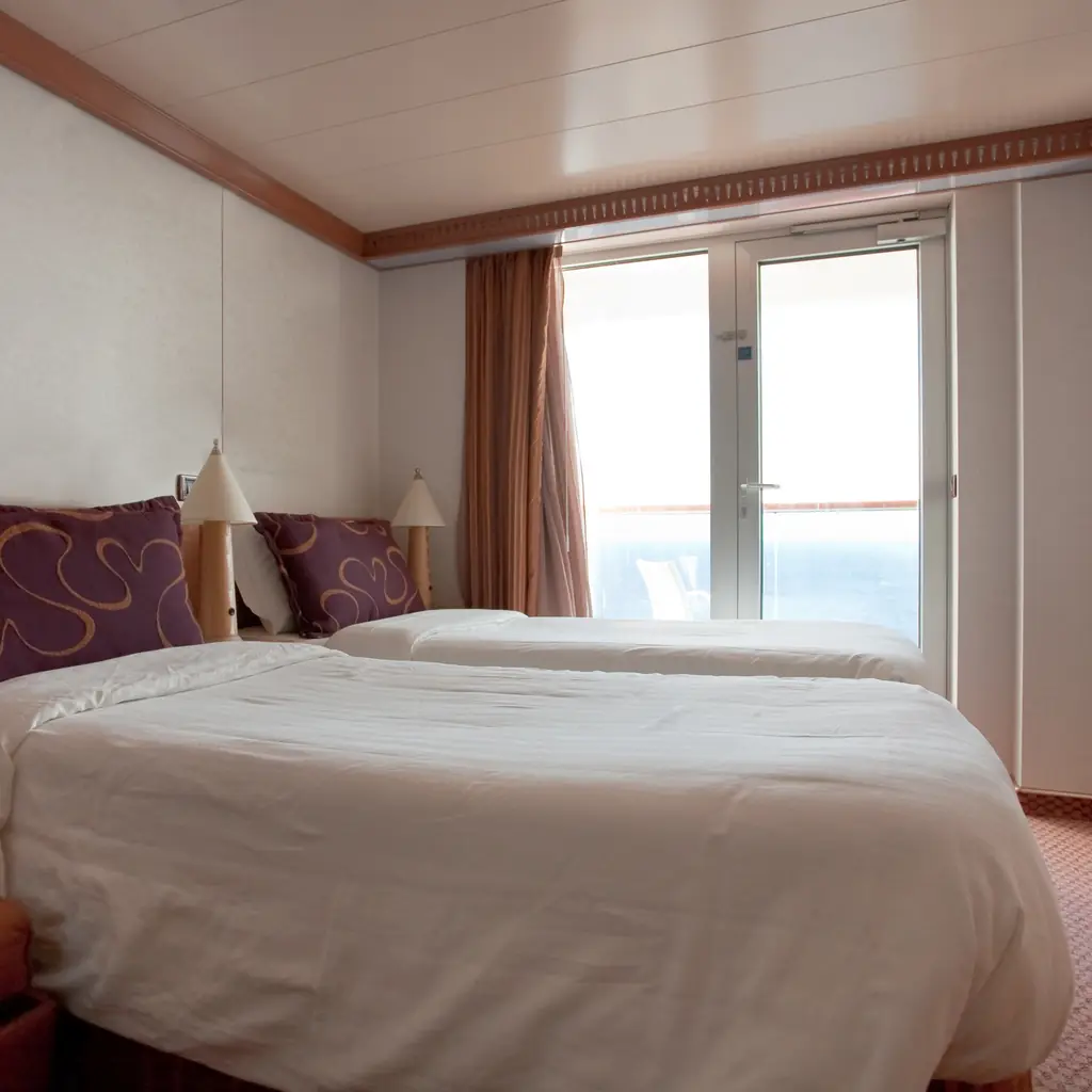 A cruise ship suite with a sitting area and an open balcony door onto the sea