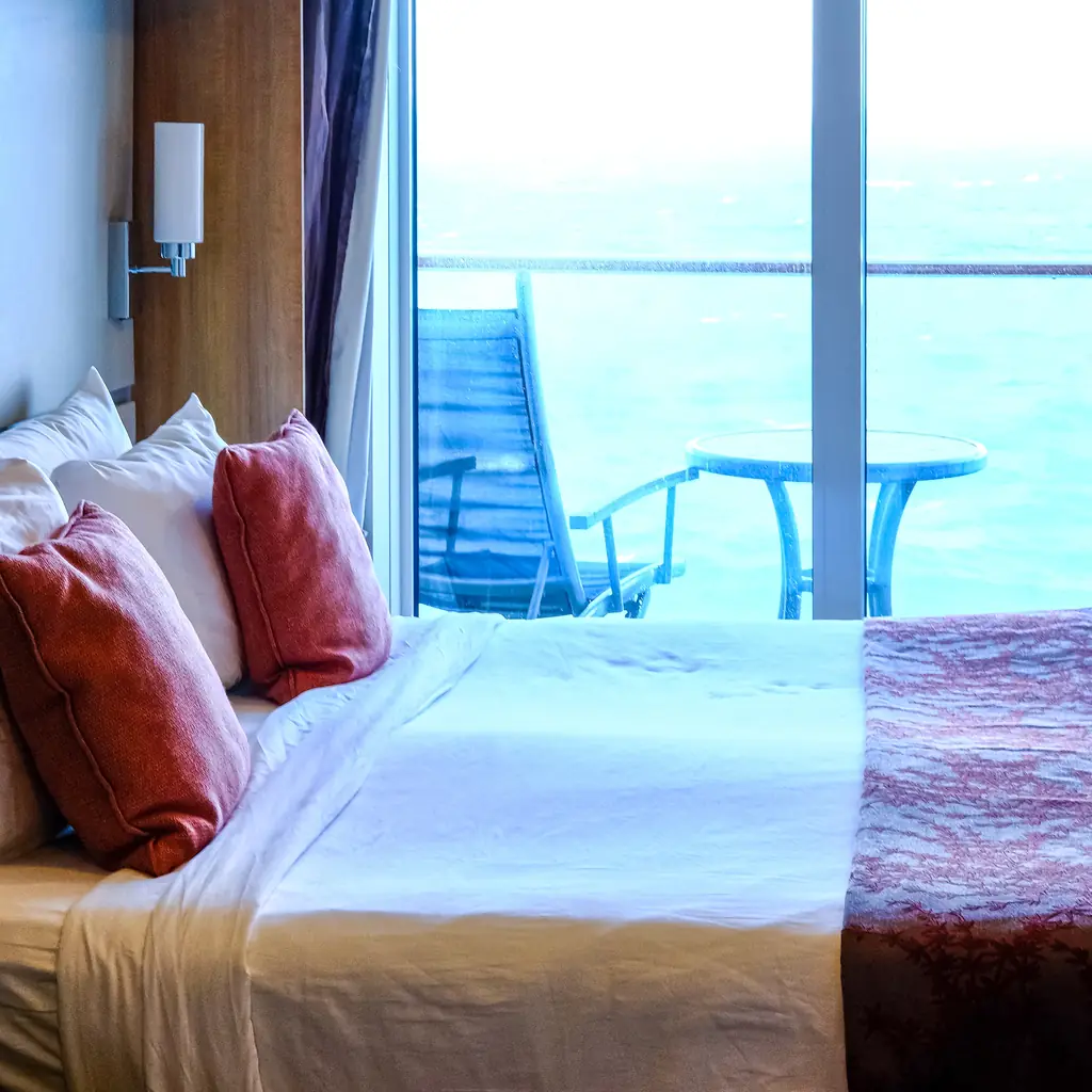 A cruise balcony cabin bed with the balcony and ocean visible, the kind of access that comes standard above an interior room.