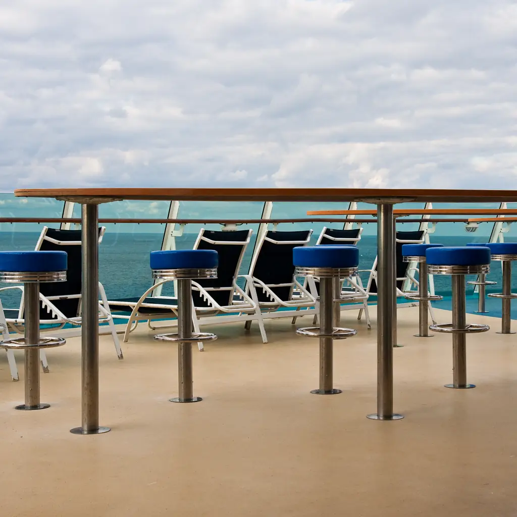 Chaise lounges and a bar area on a cruise ship deck, the kind of adults-leaning sundeck space some lines offer as a day-pass or suite perk.