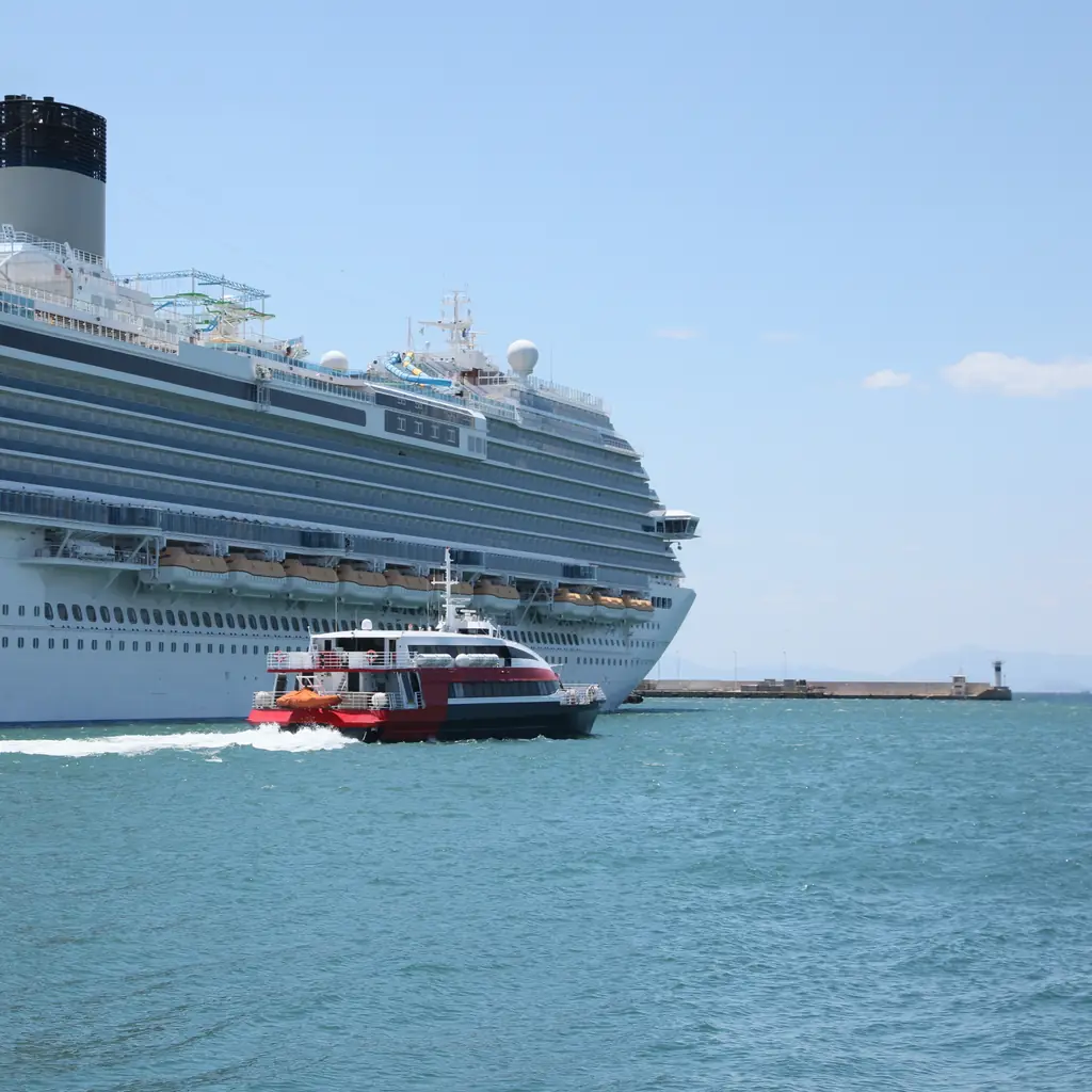 A small tender boat alongside a cruise ship, the kind of vessel used to ferry passengers to shore at anchorage ports.