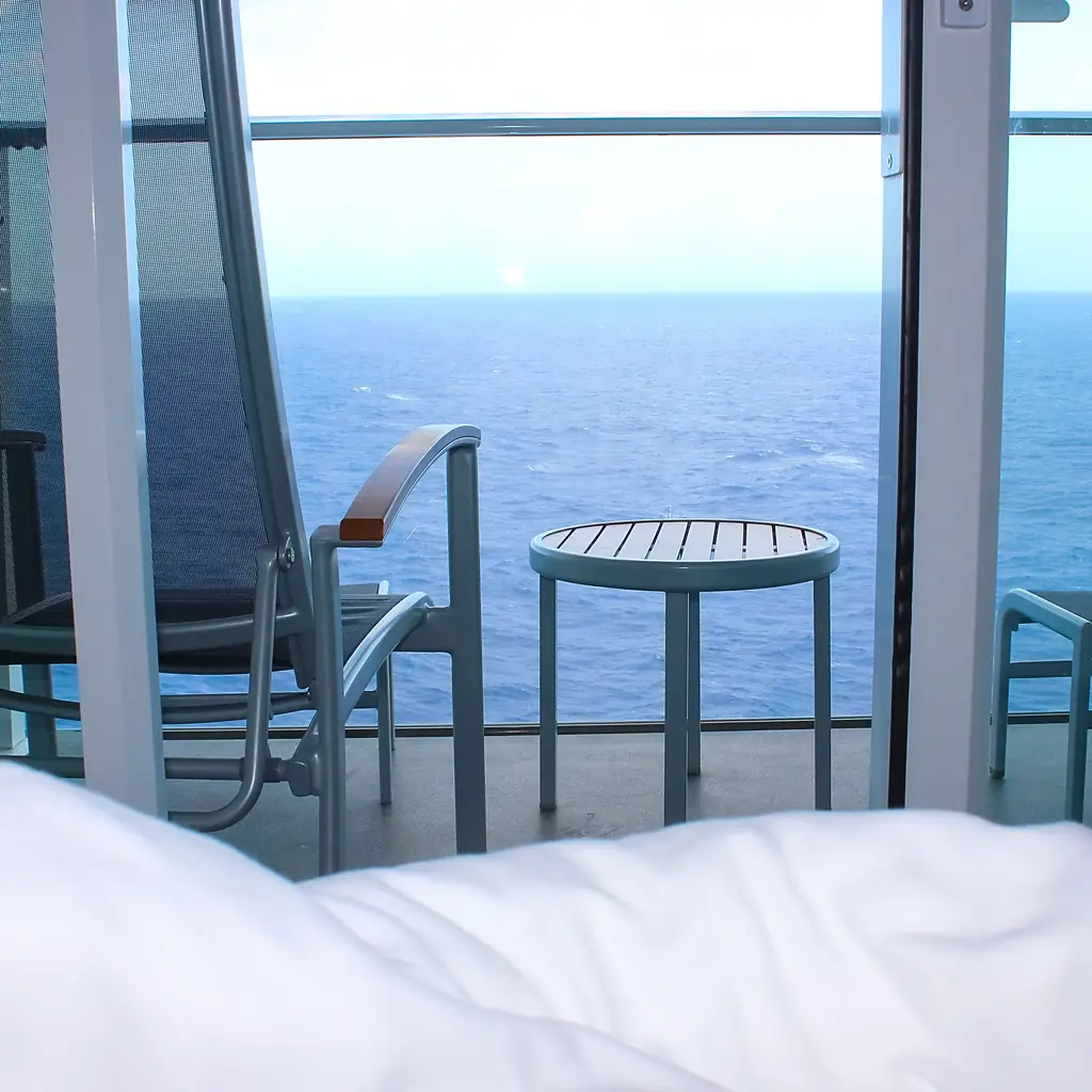 The interior of a cruise ship cabin with balcony doors open to the ocean, the kind of private enclave suite a butler-staffed program is built around.
