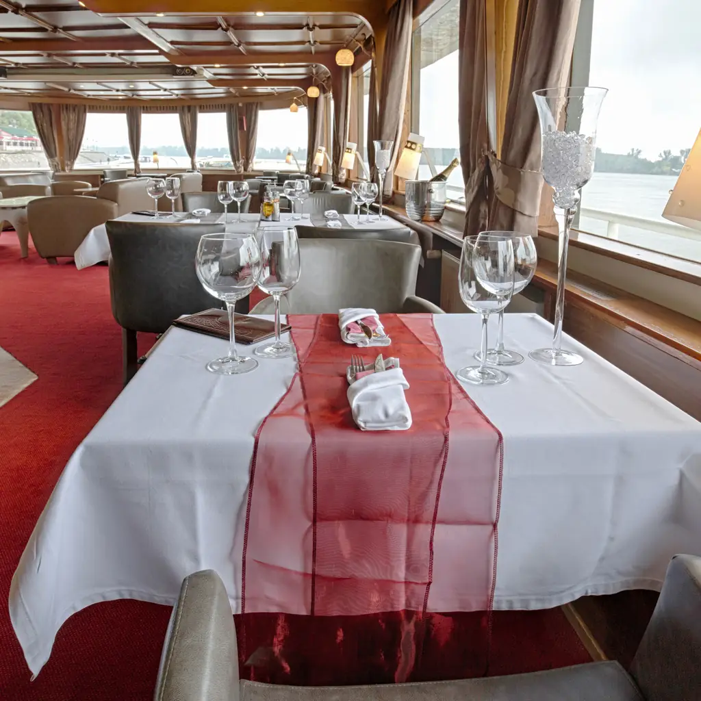 A quiet, elegantly set cruise ship restaurant dining room, the kind of suite-exclusive venue that comes with the cabin category rather than a dining package.