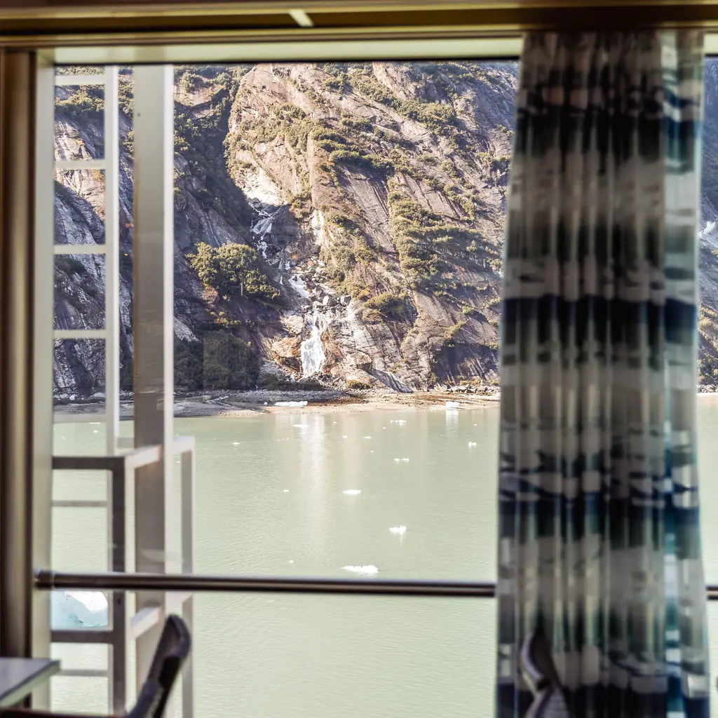 The view of Glacier Bay, Alaska, from inside a cruise ship cabin, illustrating how balcony positioning affects a glacier-day view.