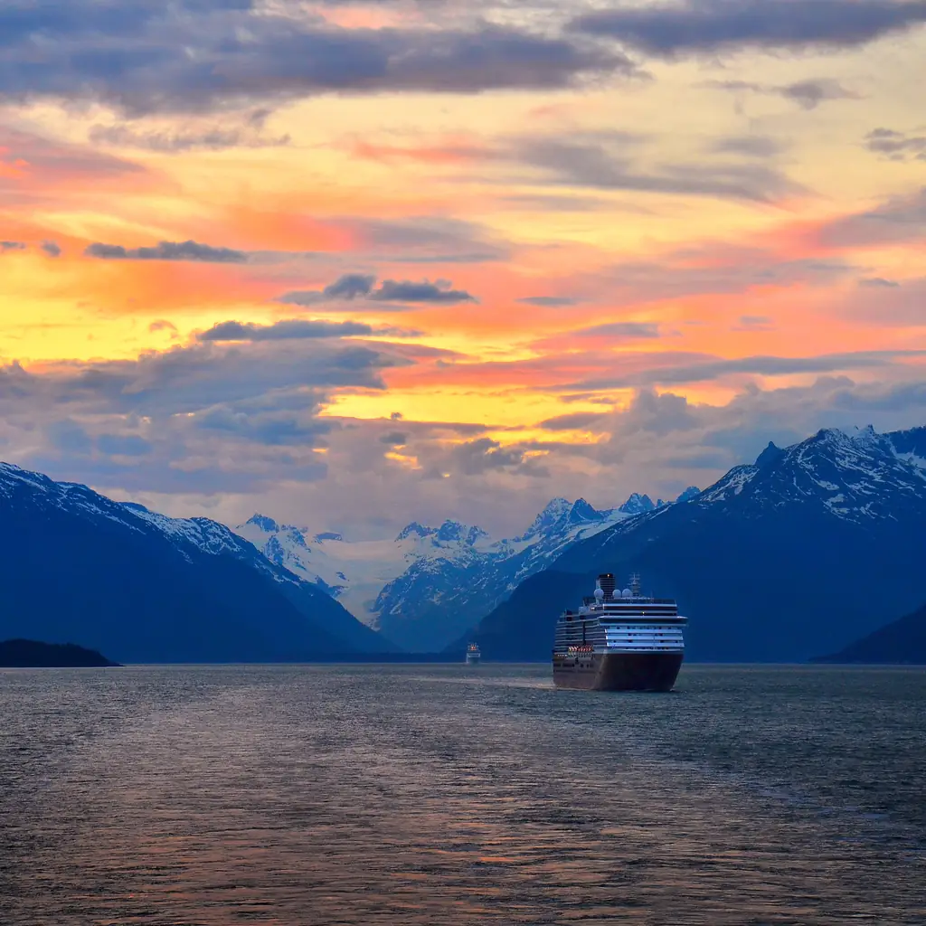 A cruise ship with Alaska's coastal mountains in the background at sunset, the kind of scenery premium suite categories are marketed around.