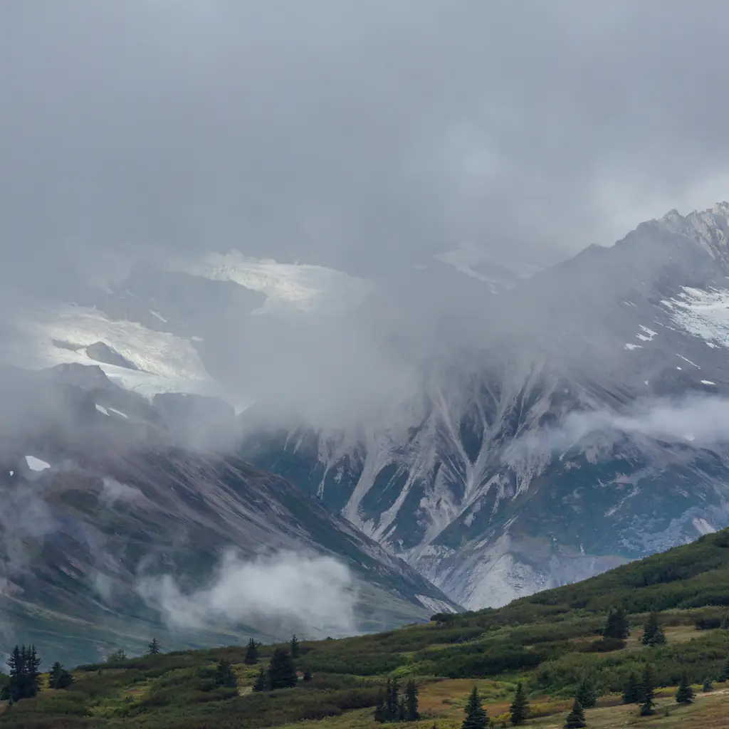 Fog partially obscuring high mountains in Alaska, illustrating that weather and visibility are never guaranteed on any tier of excursion.