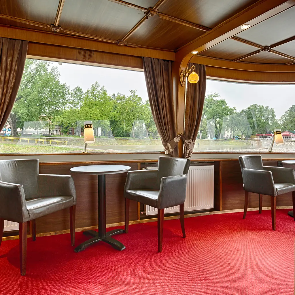 A ship lounge interior with large panoramic windows, the kind of forward observation lounge used on glacier-viewing days.