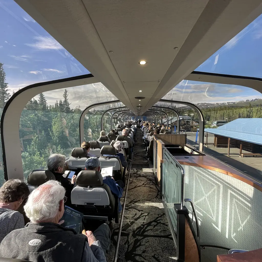 The interior of an Alaska Railroad Ultra Dome Car, showing passengers seated beneath the glass dome on a cruisetour rail route.